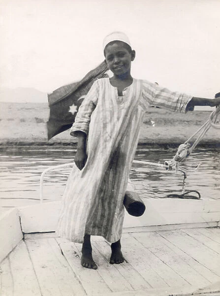 The little son of a ferryman at Luxor, Egypt, steers his fathers boat with his leg