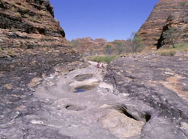 Tourists cross flood scoured rocks, past typical formations, Purnululu National Park