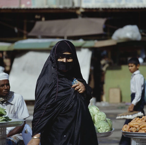 10015681. UAE Dubai Arab woman in black wearing yashmak at local market
