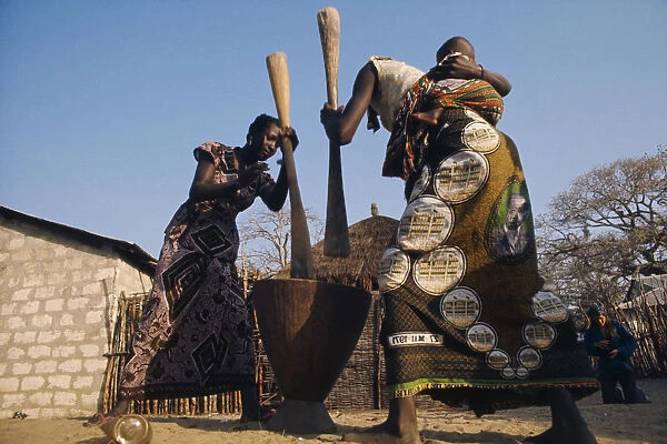 20072765. SENEGAL Agriculture Women pounding maize one carrying baby on her back