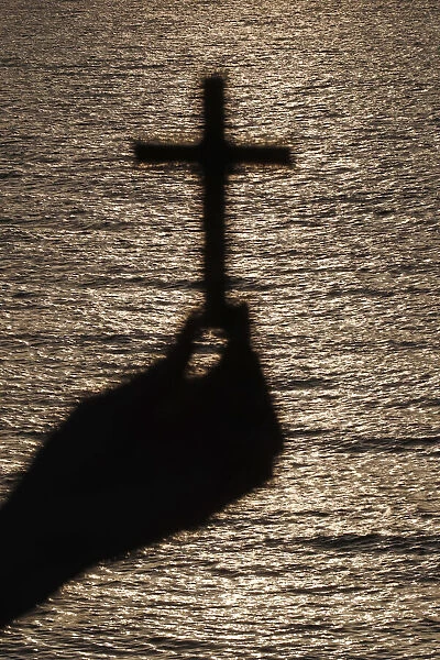 Faithful woman praying with chrisrtian cross at sunset. Close-up onn hand. Concept for religion, faith, prayer and spirituality