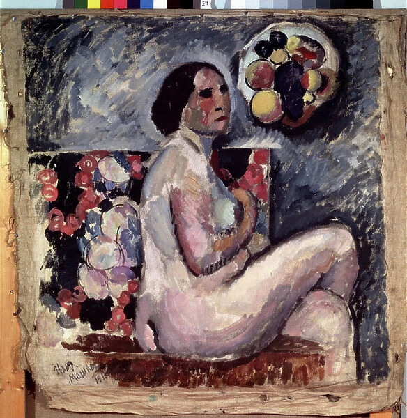 Akt. Portrait d'une femme nue, assise les jambes croisees, de profil esquissant un geste de pudeur. Derriere elle, un tableau de fruits et accroche au mur, un chapeau decore de fruits