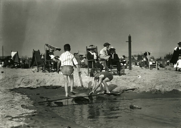 Two children play with wood scraps in shallows, Coney Island, c. 1910-21 (b  /  w photo)