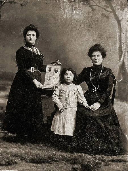 Descendancy and Genealogy: Three women of three different generations pose for a photograph with a family photo album as testimony of previous generations. Italy, circa 1890