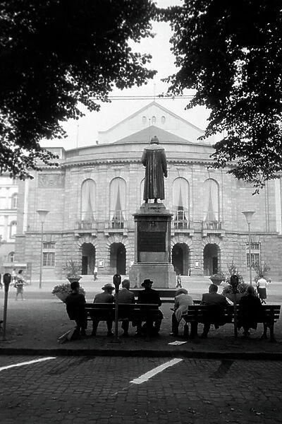 Inhabitants of Mainz sitting on benches on Gutenbergplatz square, facing the rear of the Gutenberg monument and the city theatre, Germany 1961