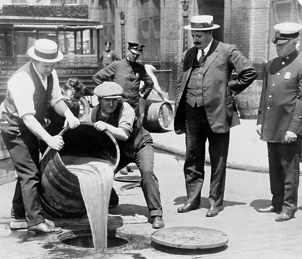 New York City Deputy Police Commissioner John A. Leach, watching agents pour liquor into sewer following a raid during the height of prohibition, c. 1921 (b / w photo)