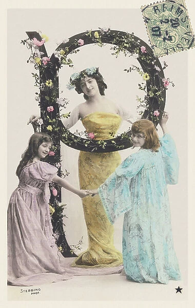 P: Capital letter decorated with flowers, a woman and two girls wearing long cloths. 1907 (photograph)