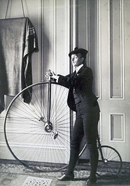 Photographic print : albumen, of photographer Frances Benjamin Johnston, full-length self-portrait dressed as a man with a false moustache, posed with Penny Farthing bicycle, facing left