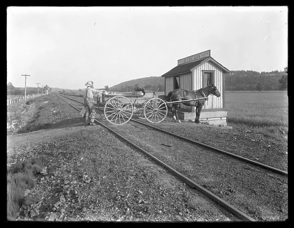 Unidentified man loading milk on to horse-drawn cart parked over railroad tracks outside