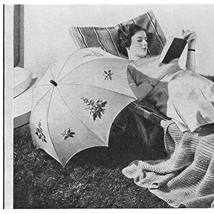 Model reading on a garden lounger with an umbrella, wearing very thick silk stockings, advertising patterns for an embroidered sunshade and knitted blanket. Date: 1935