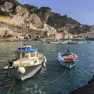 Fisherman working on harbour quayside with view towards Amalfi town and fishing boats