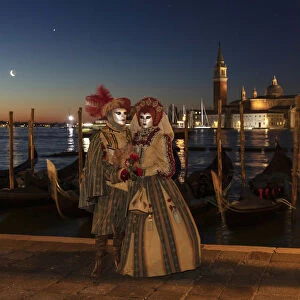 A couple in costume during the Venice Carnival posing in front of Venice lagoon, Venice