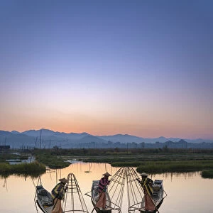 Three fishermen holding typical conical nets on their boats before sunrise