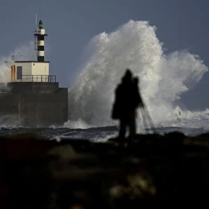 Man takes pictures of waves crashing at the San Esteban de Pravia seafront of the Spanish