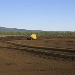 Peat extraction, tractor pulling mechanical peat extractor, working on peat bog, Sweden