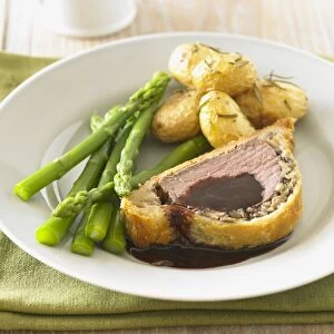 Beef Wellington served on plate with asparagus, boiled potatoes and gravy