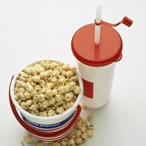 A bucket of popcorn beside a soda cup