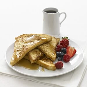 French toast, piled on a plate, topped with maple syrup and served with fresh berries, jug of maple syrup nearby, close-up