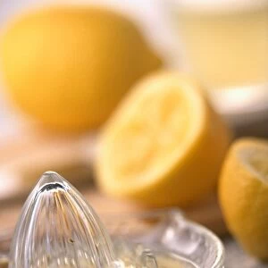 Glass lemon squeezer with lemon juice in it, lemons in background, close-up