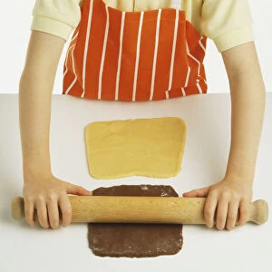 Hand model wearing orange and white striped apron, rolling out chocolate shortbread dough with wooden rolling pin