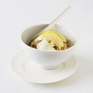 Hot apple oats topped with live natural yoghurt and apple slices, served in small, white ceramic bowl on saucer