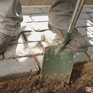 Man standing on laid brick path with spade in soil, close-up