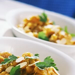 Moroccan chicken stew with saffron and apricot in a white dish, with thin slices of almonds and parsley leaves scattered on top, close-up