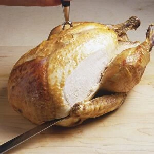Roast chicken being sliced with carving knife and fork, side view