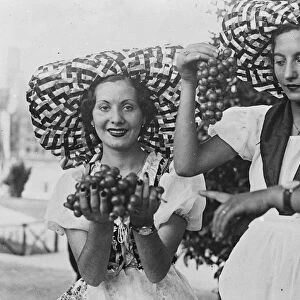 Two pretty Italian girls in peasant costume and broad brimmed hats offer bunches