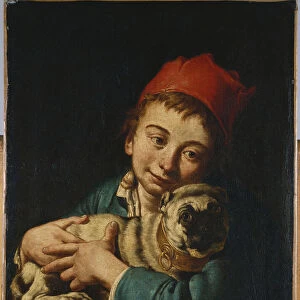 A boy, half length, in a blue jacket and a red hat, holding a pug on a cushion
