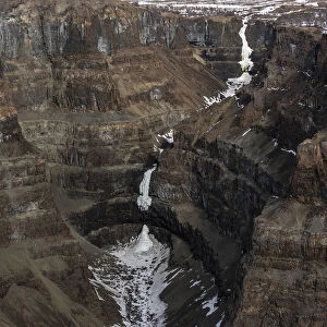 Aerial view of frozen waterfall in deep canyon in plateau, Putoransky State Nature Reserve, Putorana Plateau, Siberia, Russia. May, 2021