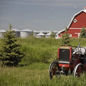Old Red Tractor In A Field With A Red Barn In The Background; Alberta, Canada