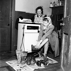 Housewife Mrs. Gladys Coates changes into better footwear after leaving the the mud
