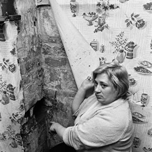 Mrs Mary Wall points out peeling wallpaper and hole in brickwork which she claims was