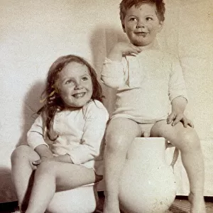 Portrait of two semi-nude children seated on potties